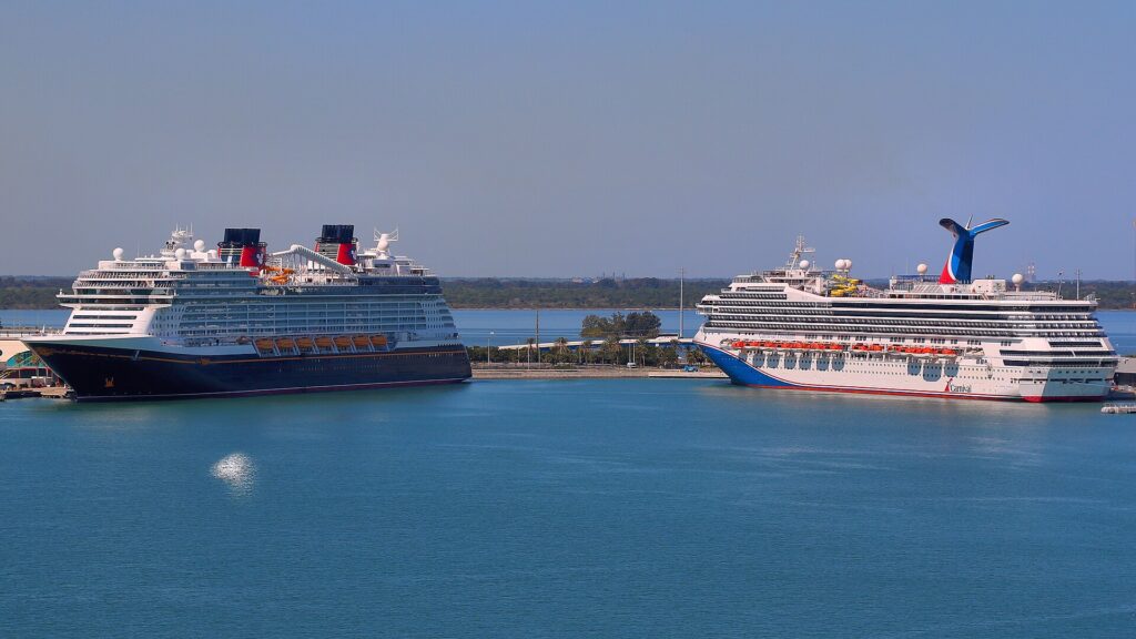 Port Canaveral: dos cruceros grandes atracados en el puerto, uno de casco azul oscuro y otro blanco con chimenea en forma de cola, sobre agua azul