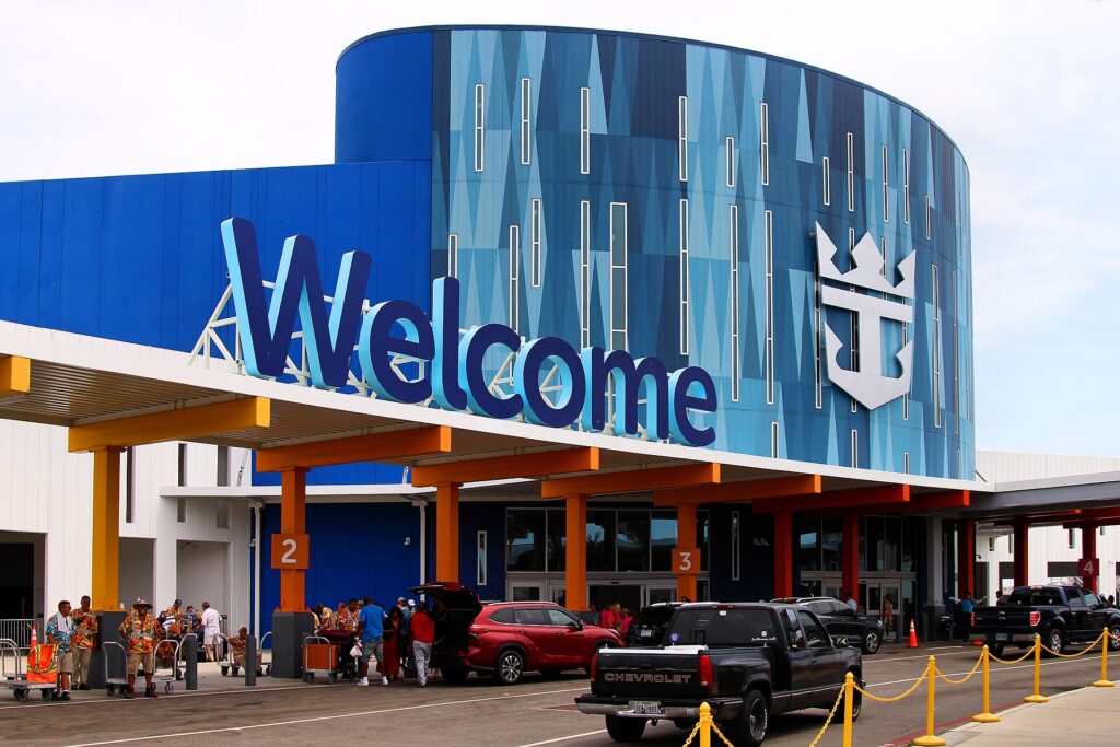 Port of Galveston: fachada azul y curva de la Terminal 10 con un gran letrero Welcome, pasajeros con maletas y autos en la entrada