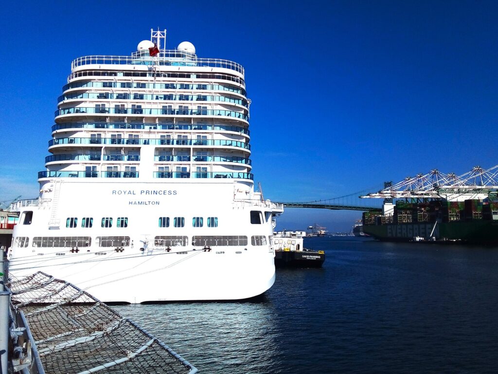 Port of Los Angeles: crucero blanco de varios pisos atracado en el World Cruise Center de San Pedro, junto a agua azul, con grúas de carga al fondo