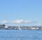 Port of Seattle: dos cruceros blancos atracados en la terminal de Smith Cove, vistos desde el agua azul de la bahía, con colinas arboladas detrás