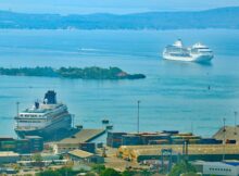 Terminal de cruceros de Cartagena: un crucero blanco atracado junto a contenedores del puerto mientras otro navega por la bahía azul, con una isla verde al fondo