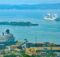 Terminal de cruceros de Cartagena: un crucero blanco atracado junto a contenedores del puerto mientras otro navega por la bahía azul, con una isla verde al fondo