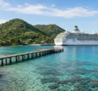 Bahía tropical de Honduras con cerros verdes, muelle de madera y arrecife, con un barco crucero blanco cerca