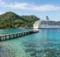 Bahía tropical de Honduras con cerros verdes, muelle de madera y arrecife, con un barco crucero blanco cerca