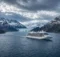 Barco crucero blanco navegando por un canal de la Patagonia entre montañas nevadas y un glaciar
