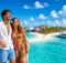 Pareja sonriente en la cubierta frente a una isla con toboganes de colores y mar turquesa