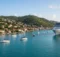Barco crucero blanco en el muelle de una bahía caribeña con casas de techos rojos, cerros verdes y veleros