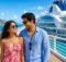 Pareja caminando por la cubierta de un crucero frente a una isla con montañas