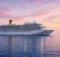 Gran barco crucero blanco navegando en un mar en calma al atardecer con cielo rosado