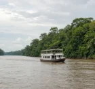 Embarcación de madera navegando por un ancho río amazónico rodeado de selva verde y neblina