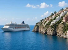 Crucero blanco navegando cerca de un pueblo costero del Mediterráneo con casas de colores sobre acantilados