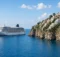 Crucero blanco navegando cerca de un pueblo costero del Mediterráneo con casas de colores sobre acantilados